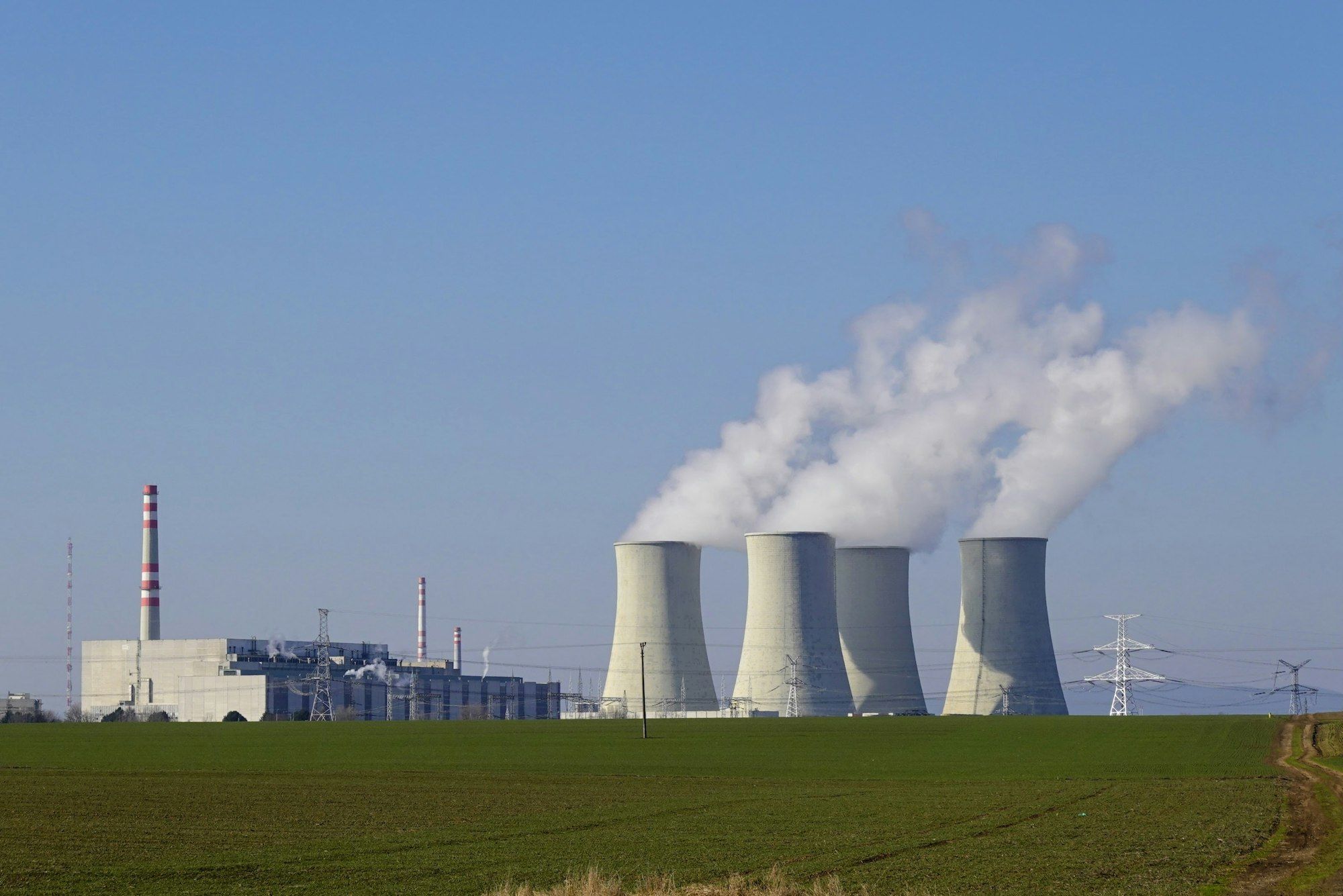 Koeltorens van een kerncentrale met stoompluimen boven een groen veld