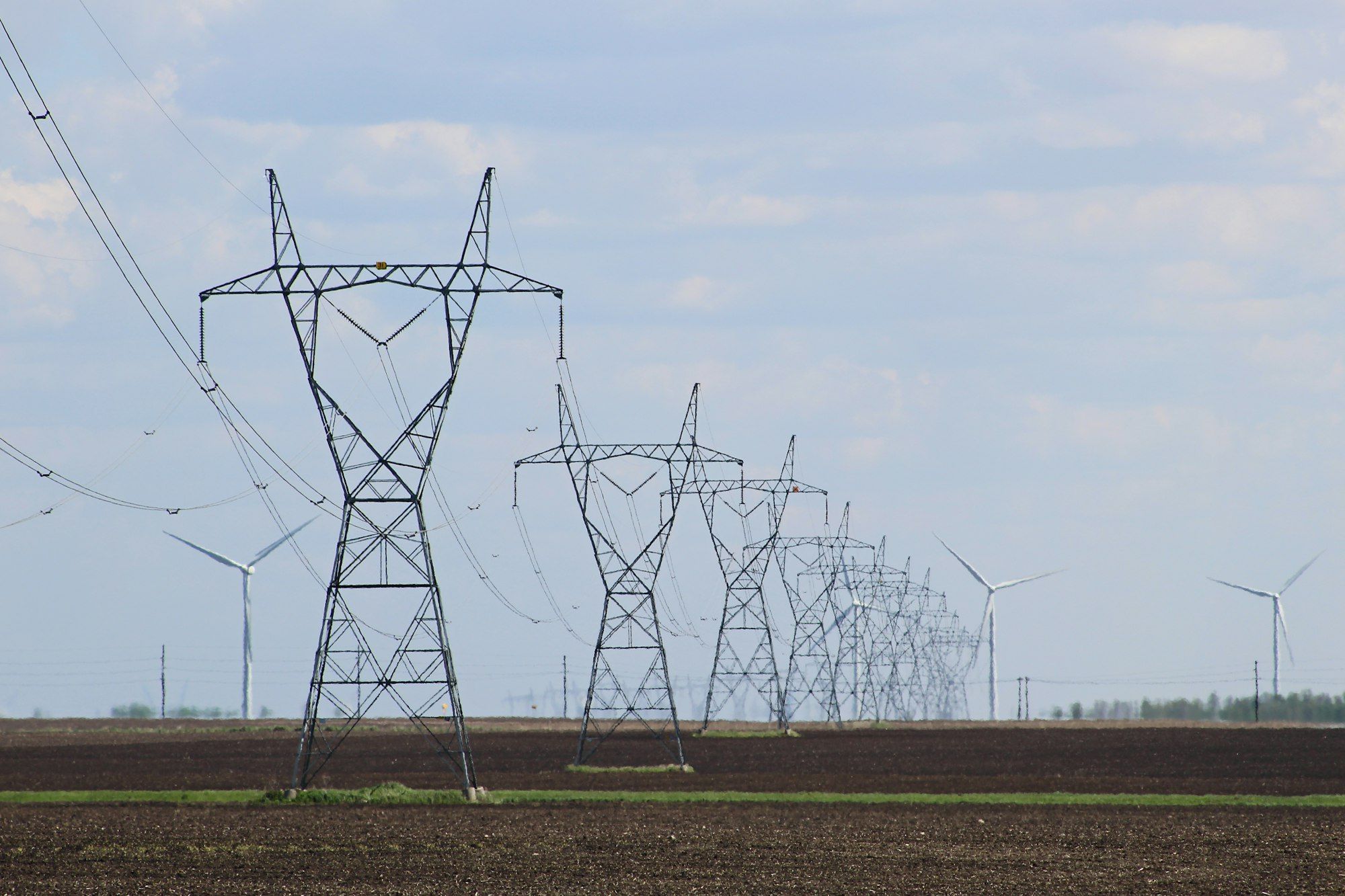 Hoogspanningsmasten over akkerland met windturbines aan de horizon